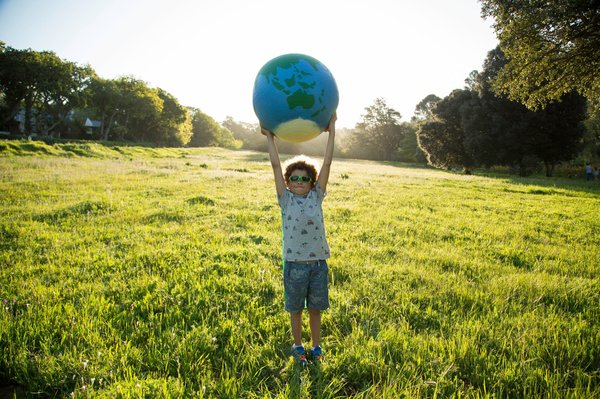 Child standing outside holding a globe above their head.